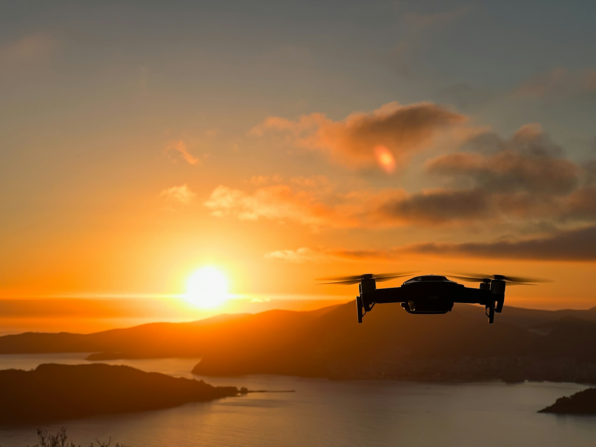 Drone hovers over the sea against the backdrop of mountains at sunset